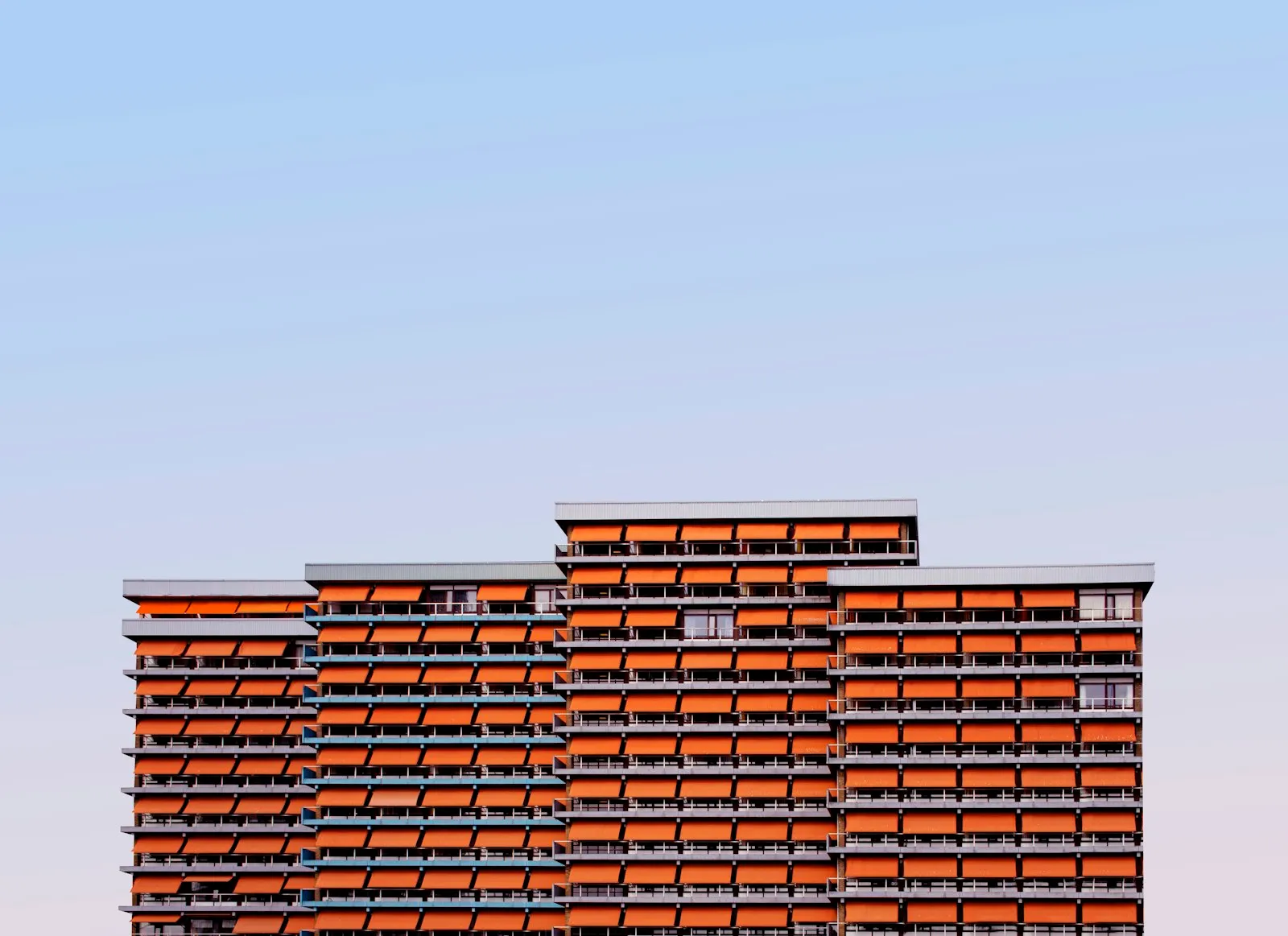 Drie moderne appartementengebouwen met oranje zonwering tegen een avondlucht