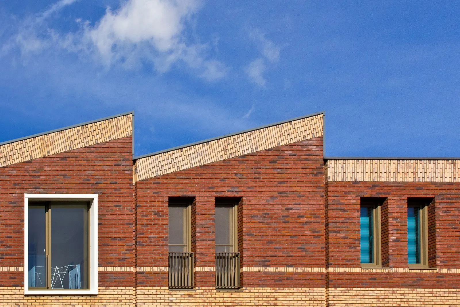 Karakteristieke roodbakstenen gevel met schuine daklijnen tegen een strakblauwe lucht — nieuwbouwarchitectuur