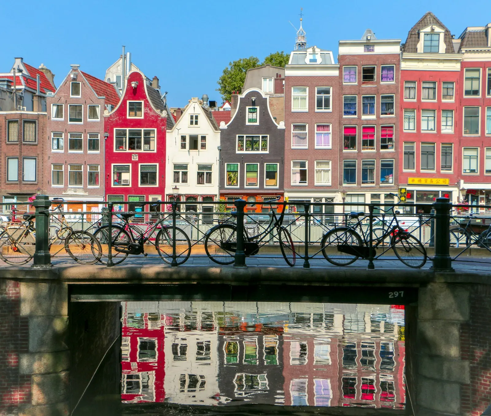Fietsen op een brug over een Amsterdamse gracht, met kleurrijke grachtenpanden en hun weerspiegeling in het water