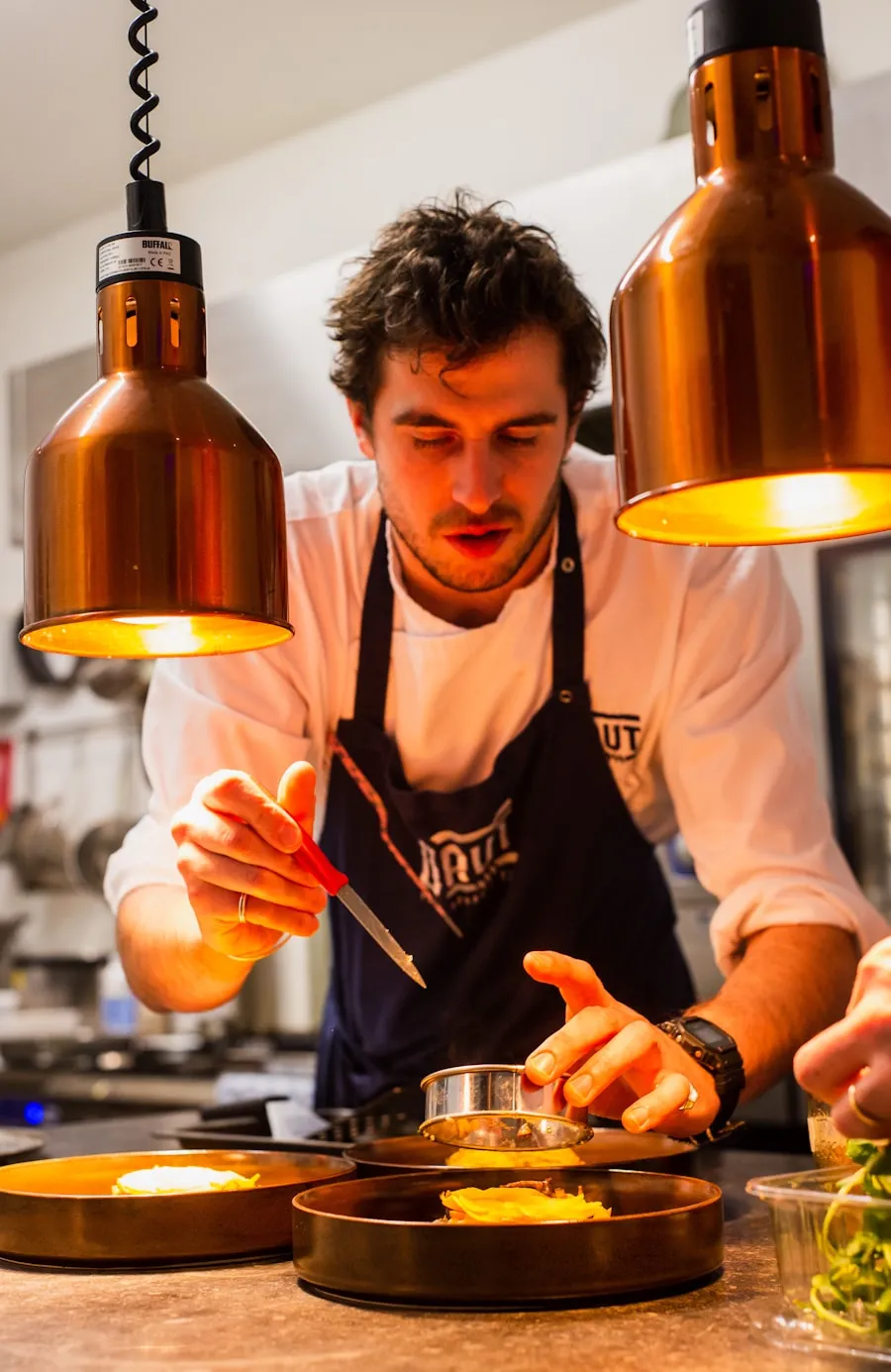 Chef Milan dresseert een bord onder de warmtelampen van Vuur