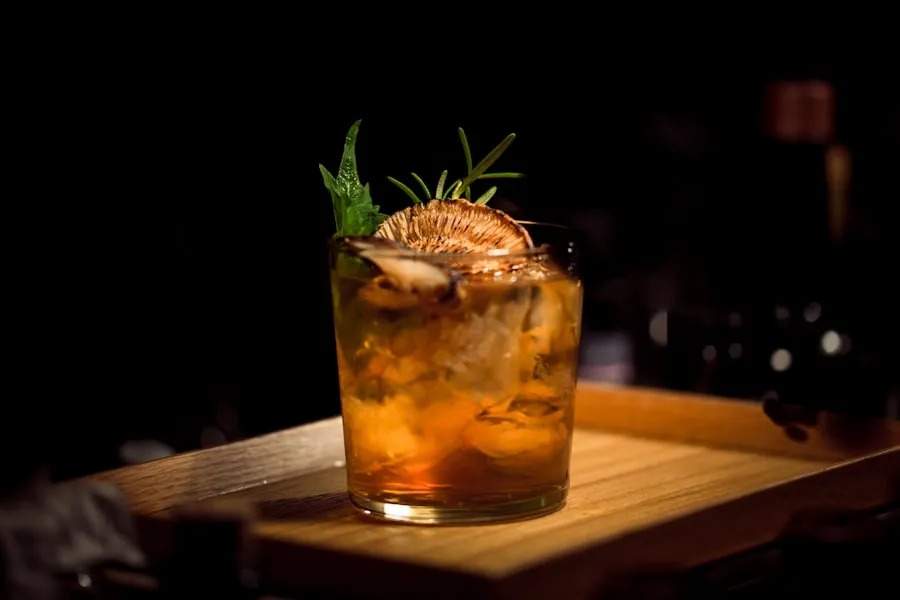 Amberkleurige cocktail met rozemarijn en gedroogde sinaasappel in kaarslicht