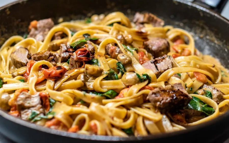 Tagliatelle met stukjes gebakken rund, tomaat en spinazie in een pan