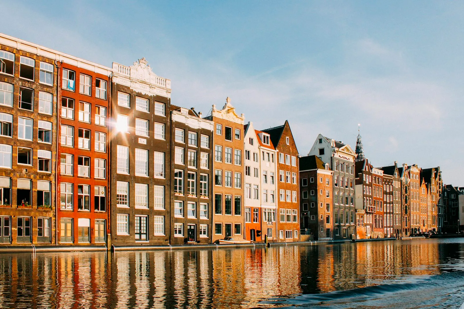 Amsterdamse grachtenpanden in warm avondlicht, weerspiegeld in het water