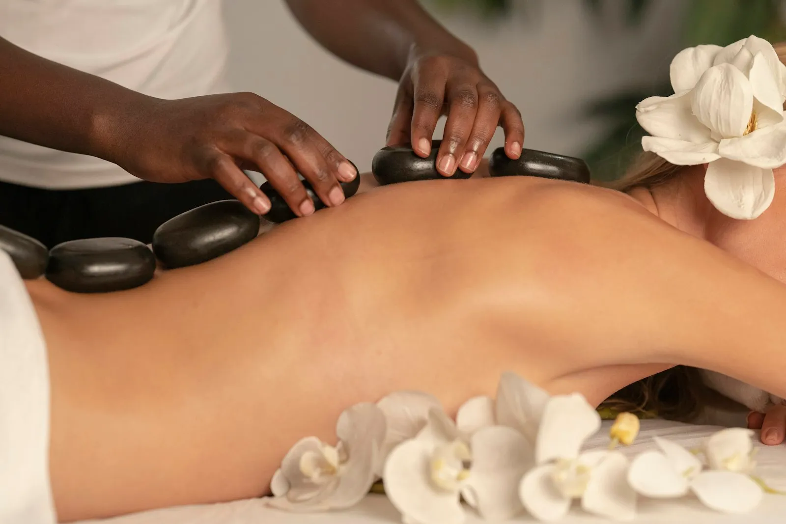 Hotstone-massage bij Studio Bloei: warme basaltstenen worden zorgvuldig op de rug gelegd, met witte orchideeën ernaast