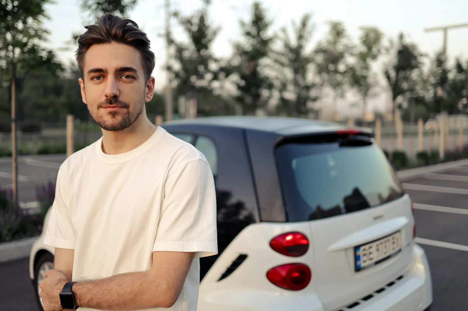 Bram Vermeulen, rij-instructeur bij Rijschool Vaart, staat met de armen over elkaar bij een lesauto op een parkeerterrein