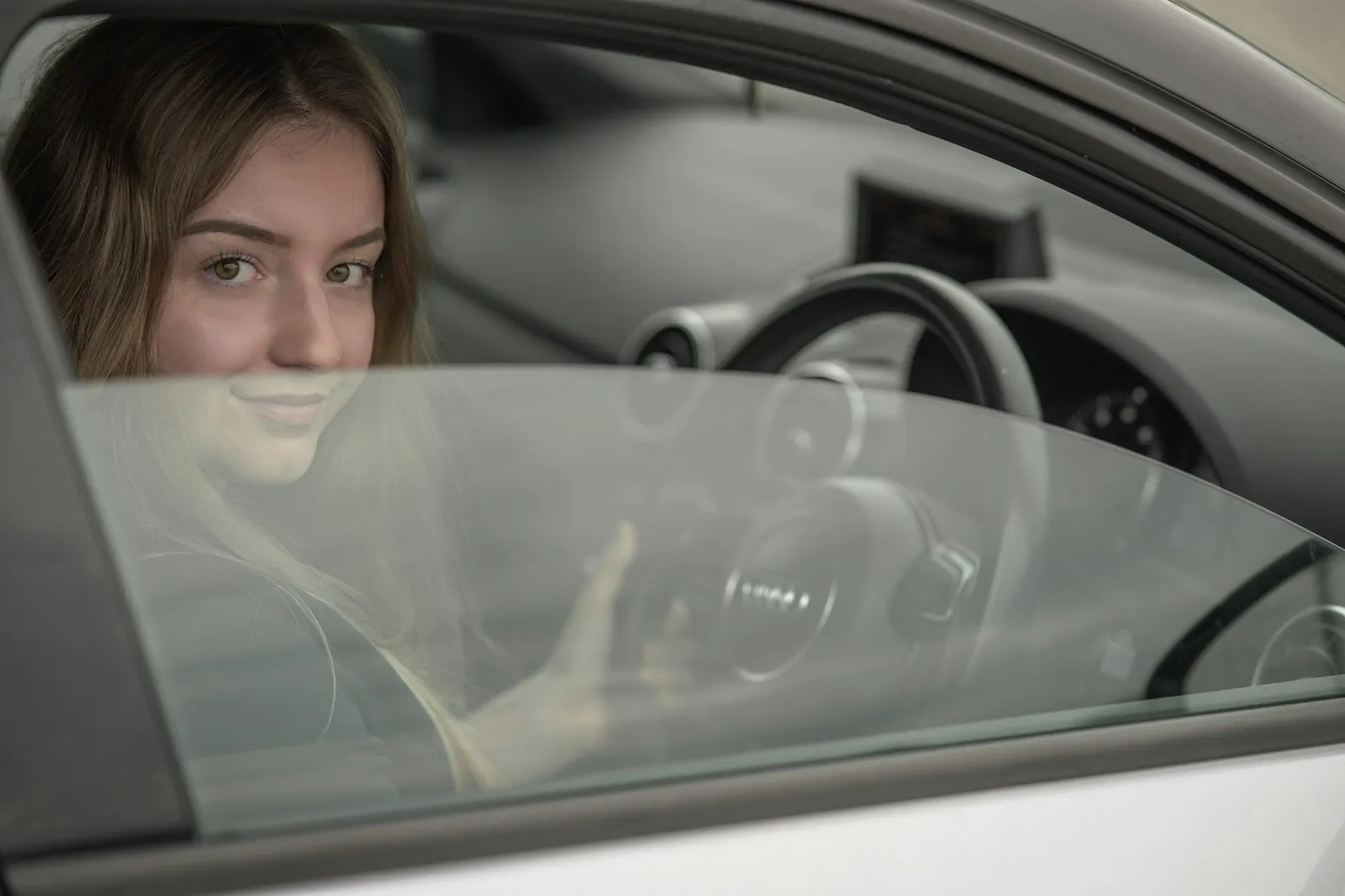 Yara Sallam, rij-instructeur bij Rijschool Vaart, kijkt glimlachend uit het raam van een witte lesauto
