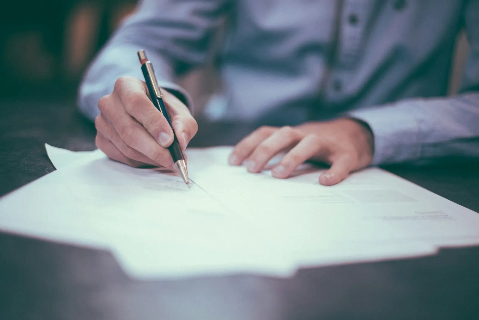 Een hand ondertekent met een pen een document op een bureau — het moment waarop de afspraken op schrift staan