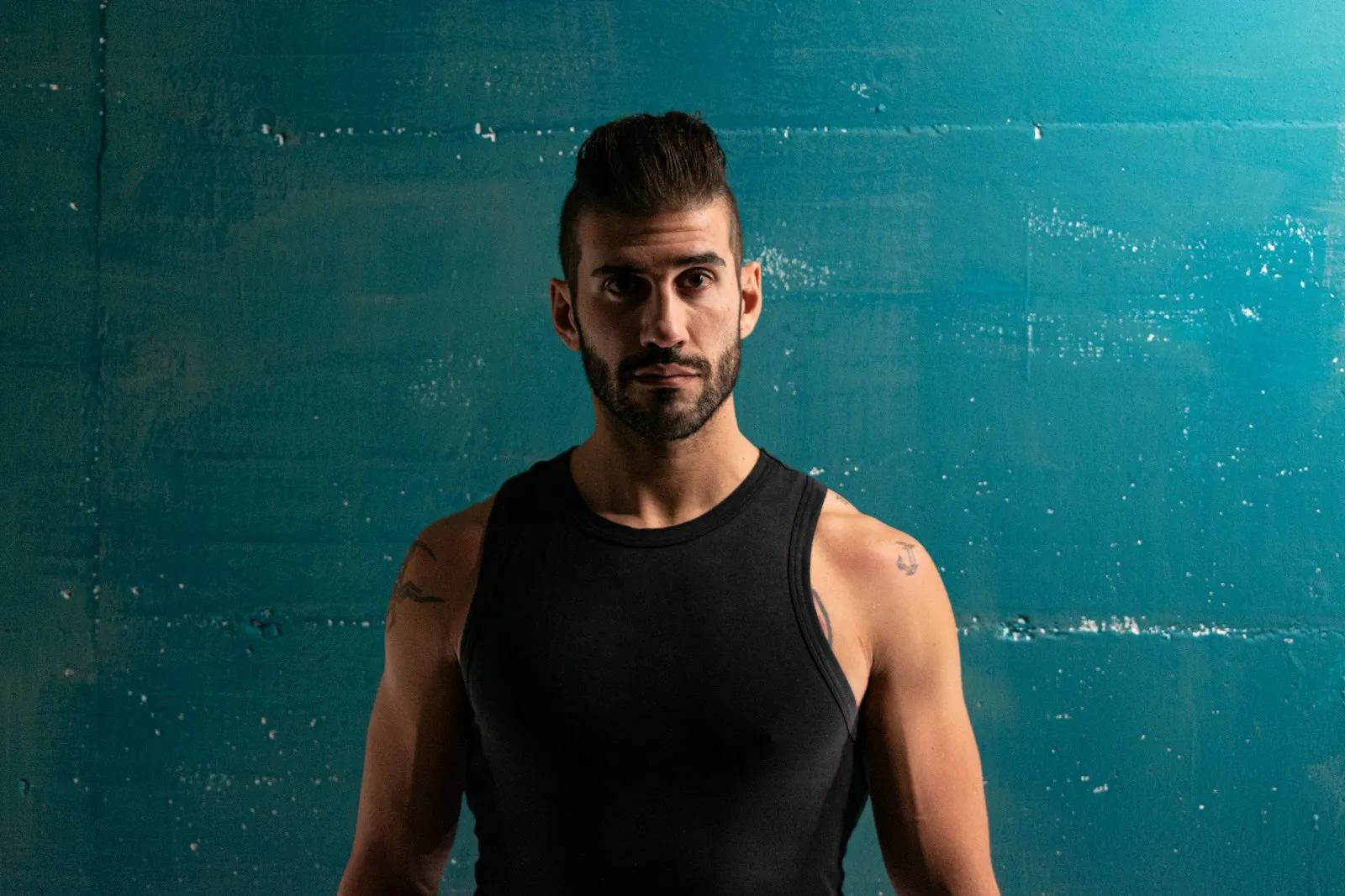 Portret van hoofdtrainer Jesse voor een blauwgroene betonwand, in zwart trainingsshirt